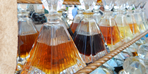 Pyramidenförmige Glasgefäße im Regal mit verschiedenfarbigen, golden und braunen flüssigen Attars darin.